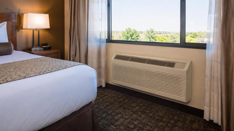 Through-the-wall PTAC air conditioner installed on a hotel guestroom wall beneath a large window