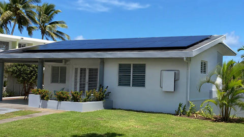 Caribbean-style home in Puerto Rico with a rooftop solar array and a wall-mounted home battery, palm trees and bright sun