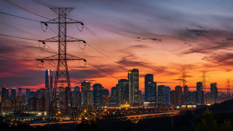 A city skyline at dusk with glowing windows and power transmission lines in the foreground