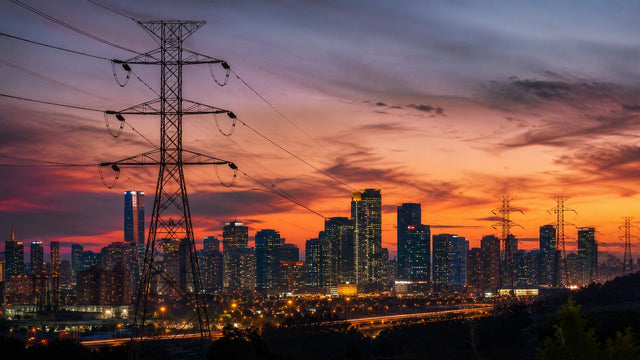 A city skyline at dusk with glowing windows and power transmission lines in the foreground