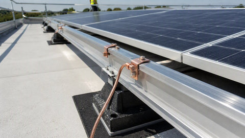 Commercial flat-roof solar array with copper grounding lugs bonding aluminum racking rails