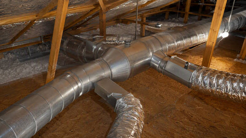 Galvanized round HVAC ducts and flex duct branching across a residential attic with foil insulation