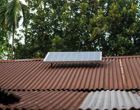 Solar panel on a rusty corrugated metal roof with green trees in the background