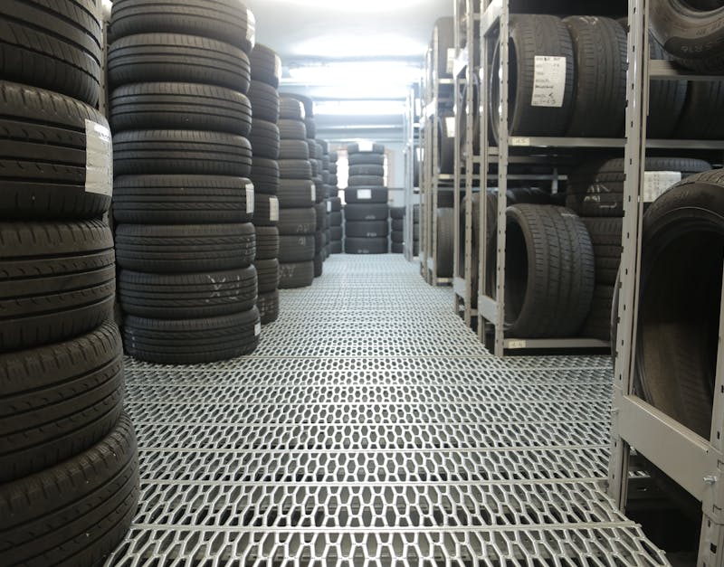 Automotive tire warehouse with stacked black car tires on metal racks and grated floor