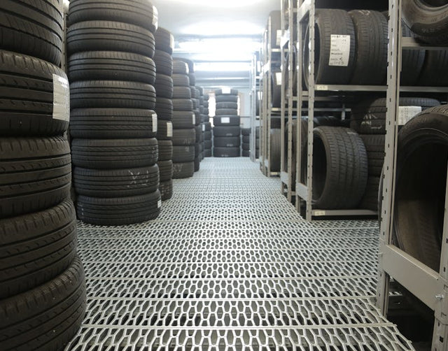 Automotive tire warehouse with stacked black car tires on metal racks and grated floor