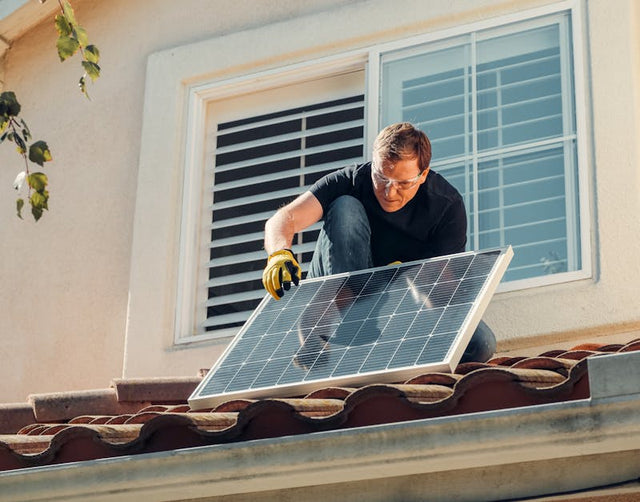 Man installing solar panel on tiled house roof near window